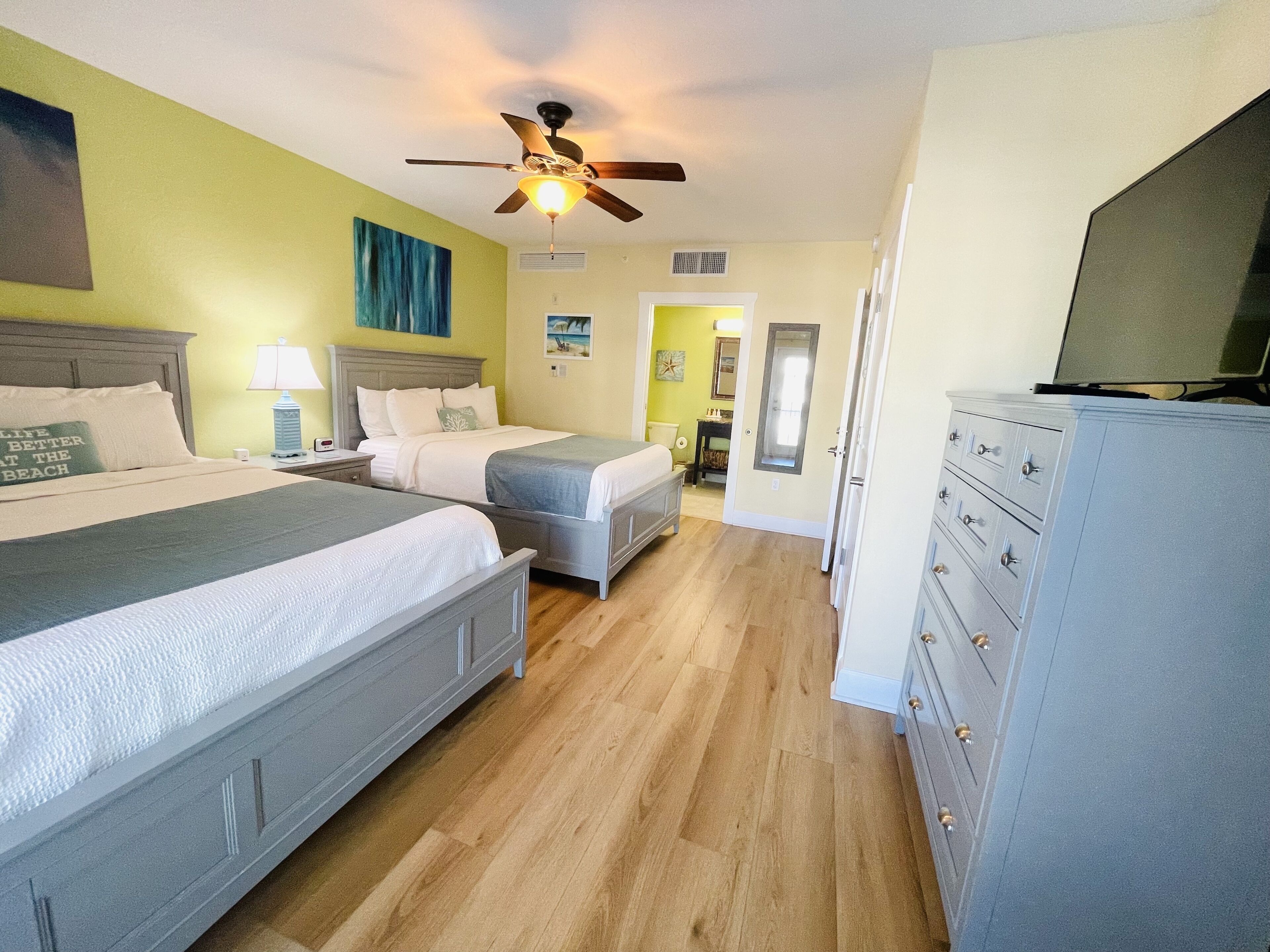 A hotel room with two beds, a ceiling fan, a TV, and a dresser.