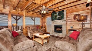Een gezellig chaletinterieur met een open haard, twee relaxfauteuils, een houten salontafel en een plafondventilator.