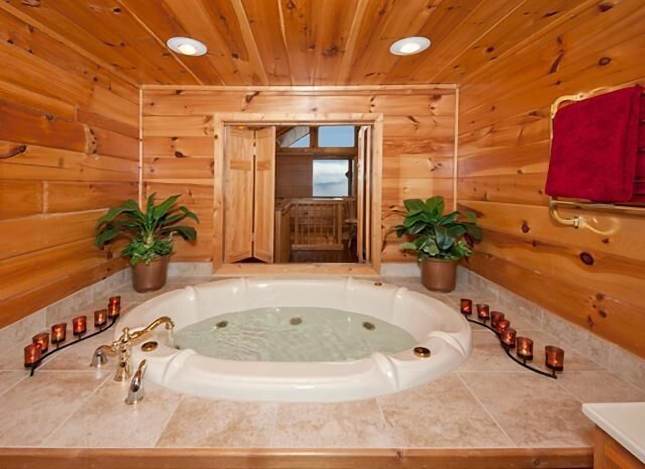 A wooden cabin with a large bathtub, two potted plants, and candles.