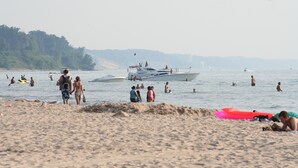 A beach with people swimming and a boat in the water.