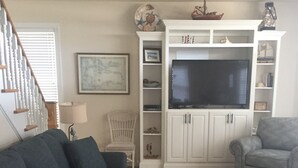 Un salon avec un canapé bleu foncé, un fauteuil gris, un meuble de télévision blanc doté d’un écran plat, et un tapis à motifs.
