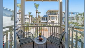 A balcony with wicker chairs, a table with a bottle and grapes, and a view of neighboring houses.