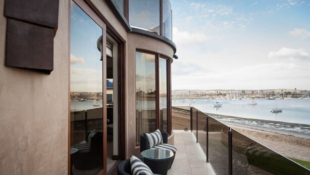 A balcony with a view of the sea and boats, featuring wicker chairs and a glass door. - Casa Ballena, Luxury On The Bay! (San Diego)