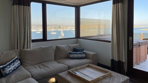 A modern living room with a sofa, a coffee table, and large windows offering a view of a marina and boats. - Casa Ballena, Luxury On The Bay! (San Diego)