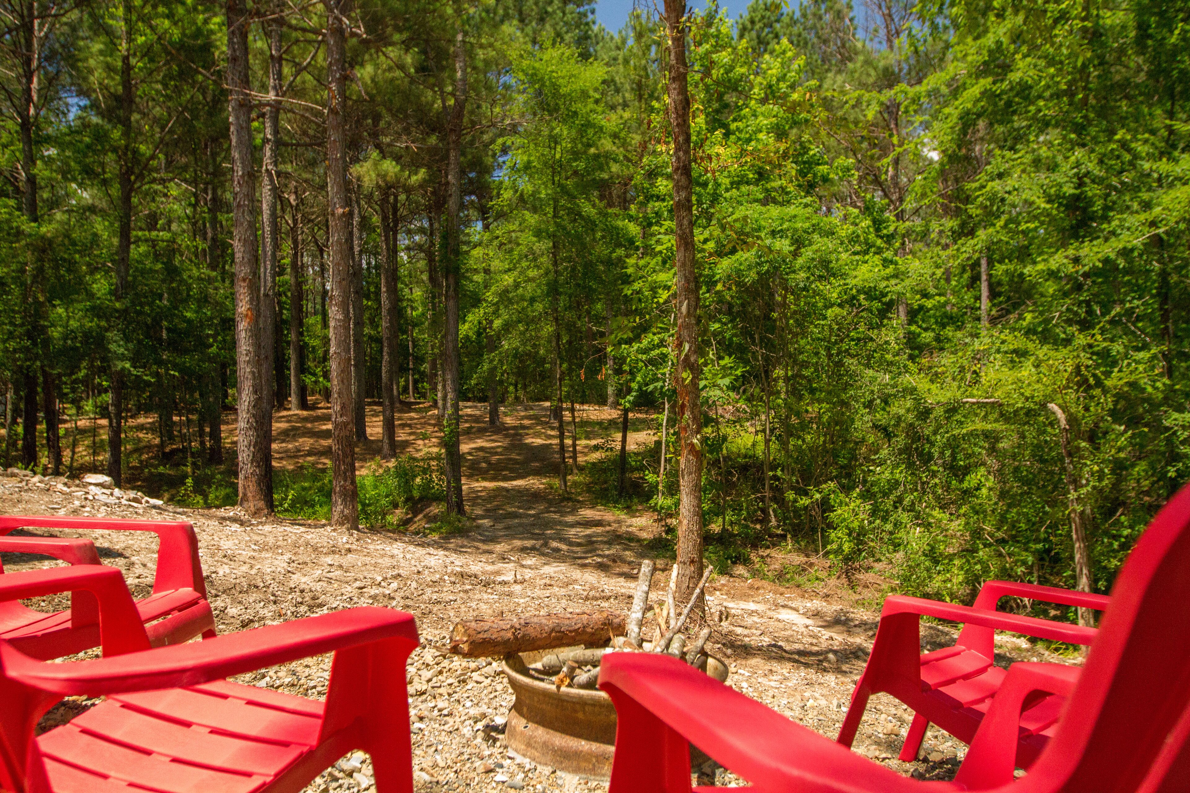 A forested area with red chairs and a fire pit.