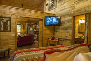 A cozy log cabin room with a bed, a television mounted on the wall, and a small table with a lamp. - Beavers Bend State Park entrance 259A , Southern Hill Addition; Wood Knot Cabin (Broken Bow)