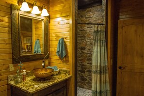 A wooden cabin bathroom with a stone wall, a large mirror, and a wooden door. - Beavers Bend State Park entrance 259A , Southern Hill Addition; Wood Knot Cabin (Broken Bow)