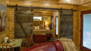 A cozy cabin interior with a wooden interior, a dining area with a table and chairs, a red leather couch, and a bedroom with a bed and a window. - Beavers Bend State Park entrance 259A , Southern Hill Addition; Wood Knot Cabin (Broken Bow)