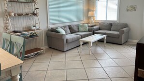 A living room with two grey sofas, a white coffee table, and a metal shelf with decorative items. - 30 Steps to Sand and Water! Panoramic Sunset and Water Views! Serenity! Pier! (Navarre)