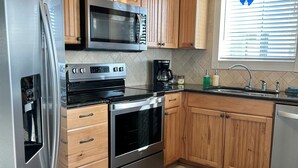 A modern kitchen with wooden cabinets, stainless steel appliances, and a window with blinds. - 30 Steps to Sand and Water! Panoramic Sunset and Water Views! Serenity! Pier! (Navarre)