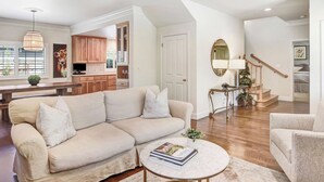 Un salón amplio con un sofá seccional color beige, una mesa de centro redonda y una escalera que sube a un nivel superior.
