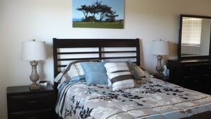 Ein Schlafzimmer mit einem Bett, zwei Nachttischen, einem Schminktisch, einem Spiegel und einem Bild an der Wand.