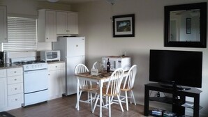 Eine kompakte Küche mit weißen Geräten, einem Esstisch mit Stühlen, einem Deckenventilator und einem Flachbildfernseher auf einem Schrank.