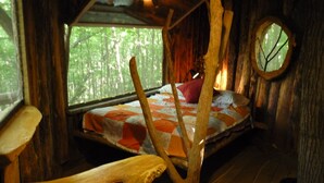 Una habitación de cabaña rústica con una cama, un ventanal redondo y un banco.