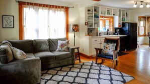A living room with a sofa, a patterned rug, and a kitchen area with cabinets and appliances.