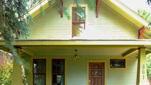A yellow house with a porch, wooden chairs, a bench, and a stone pathway leading to the door.