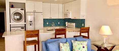 Un espacio habitable compacto con kitchenette, un sofá con cojines estampados y un comedor con sillas.