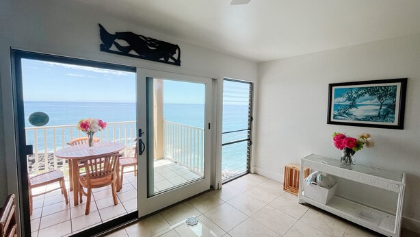 Una habitación con vistas al mar, un comedor con mesa y sillas, una consola blanca con un jarrón de flores y un cuadro en la pared.