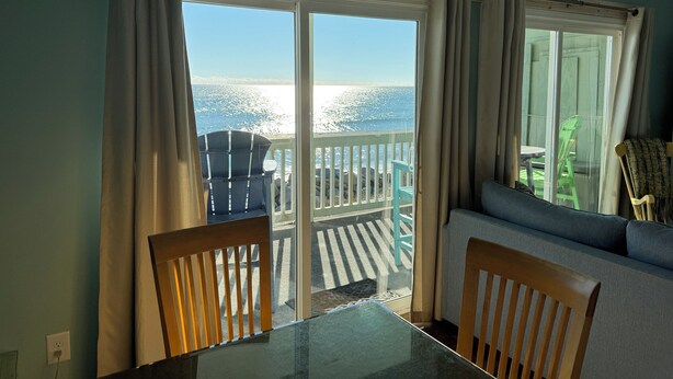 A room with a view of the ocean, a balcony with chairs, and a table. - Beach, Please: Best View of the Ocean with the Comforts of Home. 2bd/2ba (Carolina Beach)
