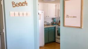 A kitchen with white cabinets, a teal countertop, and a kitchen island. There is a framed sign on the wall that says "this is my happy place." - Beach, Please: Best View of the Ocean with the Comforts of Home. 2bd/2ba (Carolina Beach)