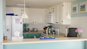 A kitchen with white cabinets, a blue countertop, a toaster, a kettle, and two wooden stools. - Beach, Please: Best View of the Ocean with the Comforts of Home. 2bd/2ba (Carolina Beach)
