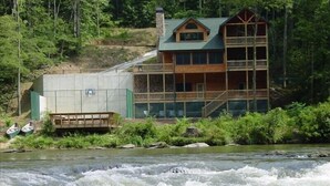 Eine Lodge mit mehrstöckiger Struktur, einem Balkon und einem Fluss davor.