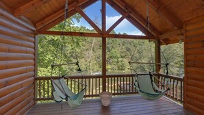 Eine Holzhütte mit Veranda, zwei Hängematten und Blick auf einen Fluss.