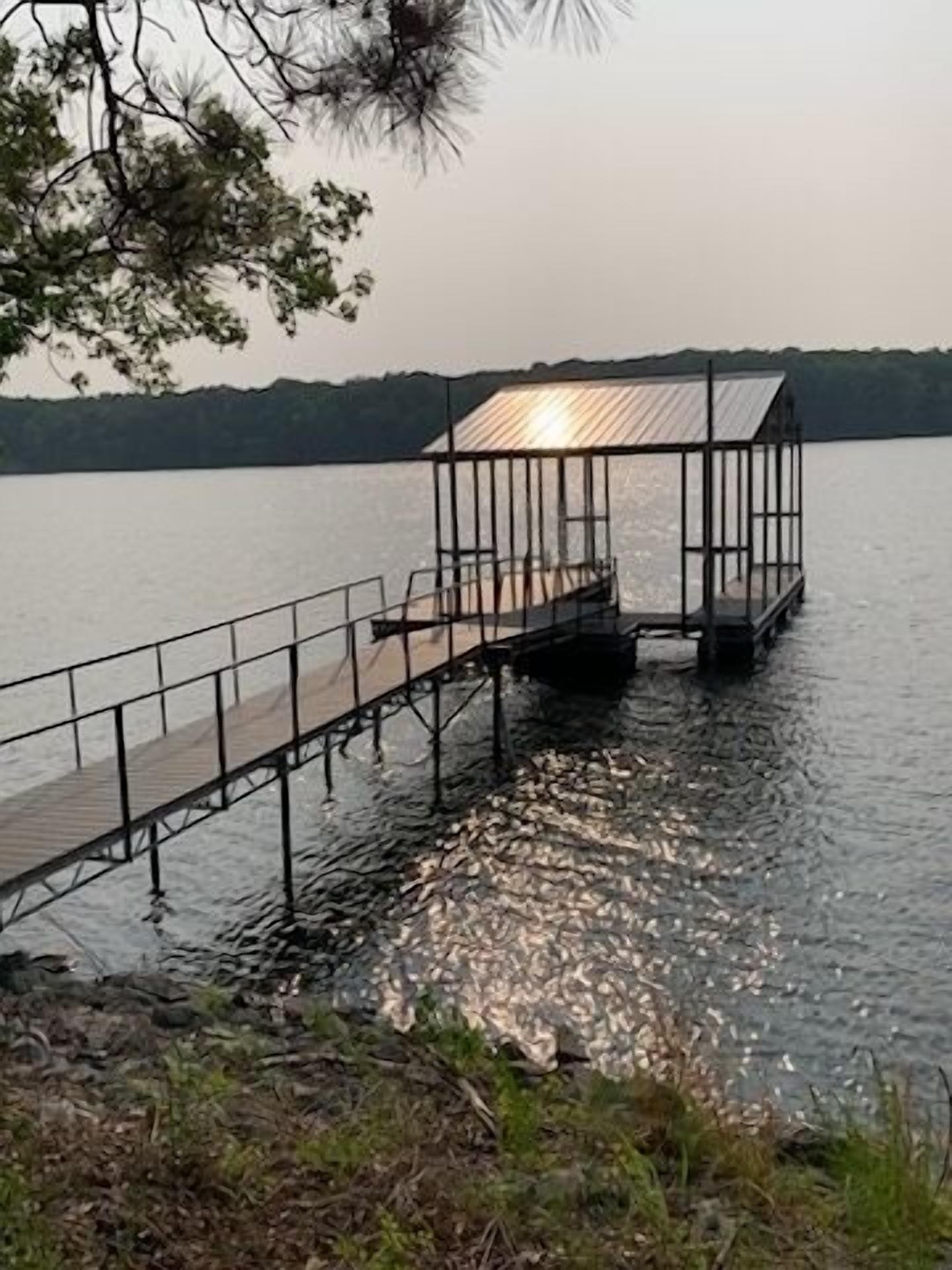 Un muelle de madera que se adentra en un lago, con barandilla de metal y una zona cubierta.