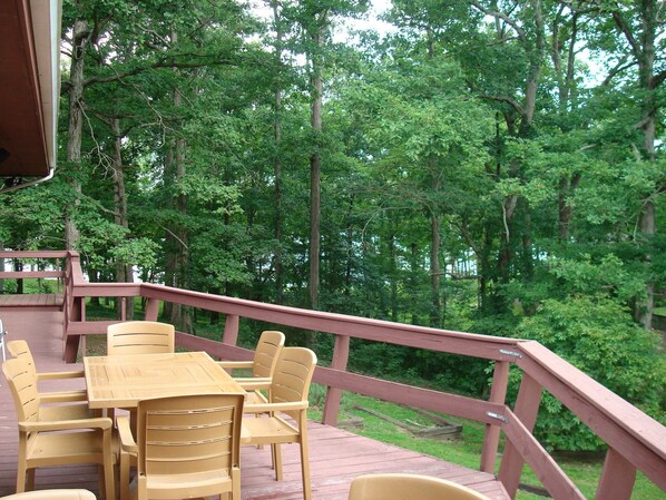 A wooden deck with a table and chairs, surrounded by a forest. - Kentucky Lake House on Jonathan Creek (Benton)