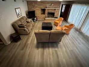 A living room with a brick fireplace, a sofa, an ottoman, and two armchairs. - Kentucky Lake House on Jonathan Creek (Benton)
