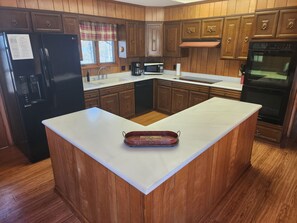 A kitchen with wooden cabinets, a black refrigerator, a microwave, a coffee maker, and a built-in oven. - Kentucky Lake House on Jonathan Creek (Benton)