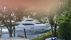 A yacht docked at a marina with a hammock, lounge chairs, and a table with glasses.