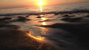 A beach scene with the sun setting over the ocean, creating a calm and reflective atmosphere.