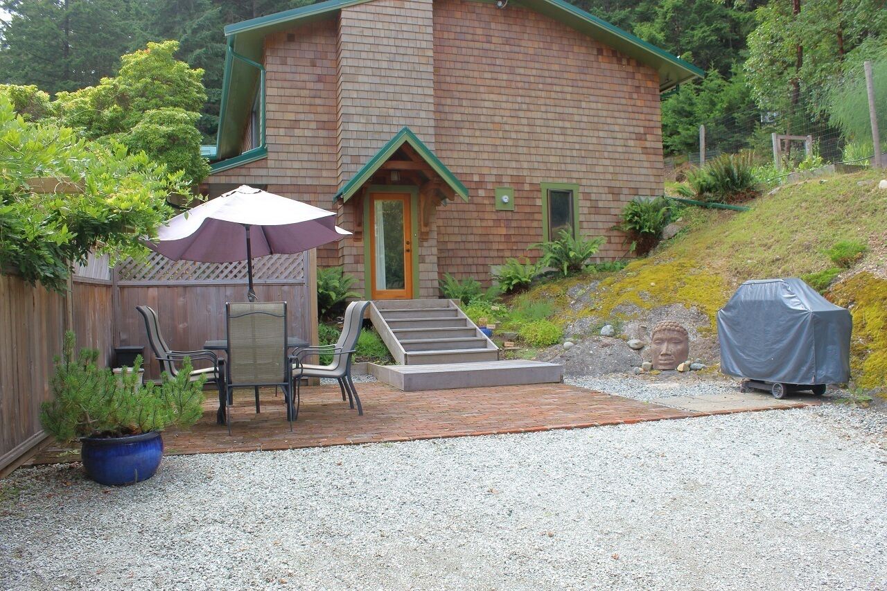 A wooden house with a covered patio, outdoor seating, and a small statue.