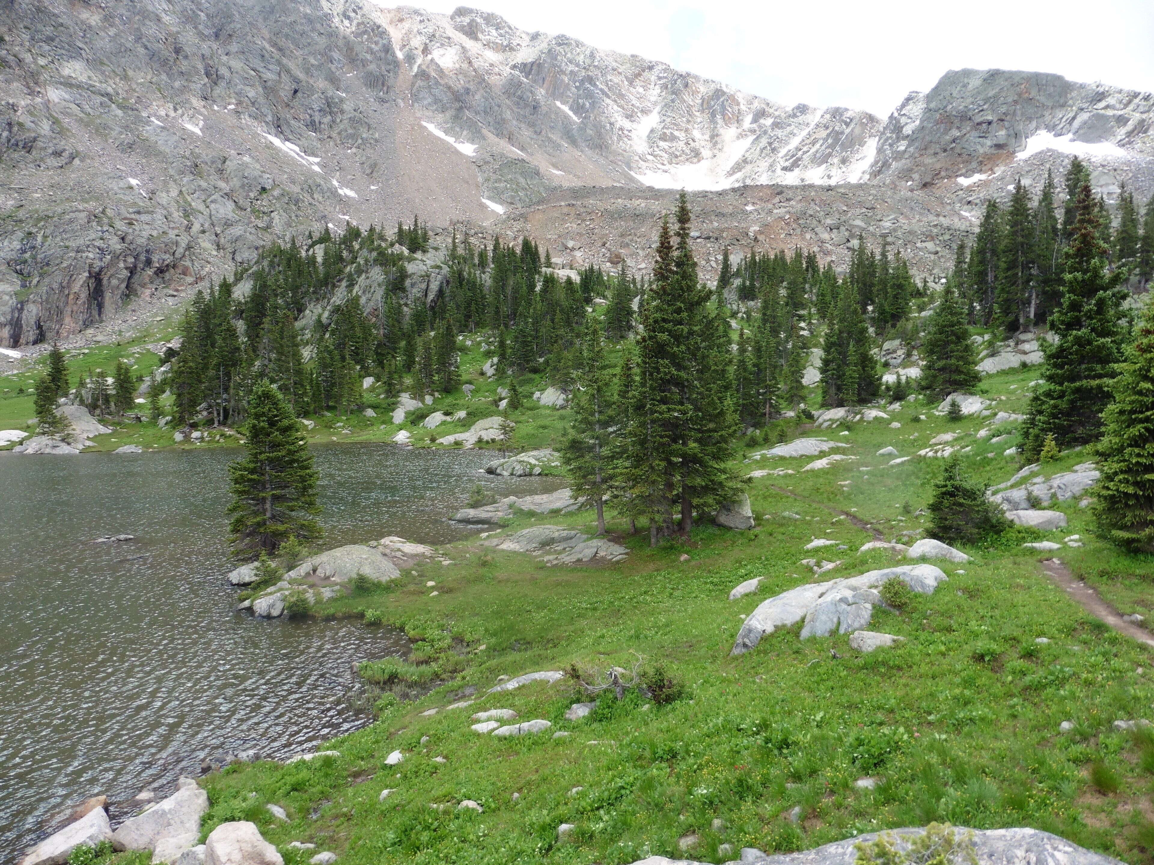 A mountainous landscape with a lake, rocky terrain, and scattered trees.
