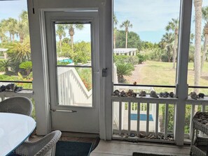 Een kamer met een glazen deur die uitkomt op een balkon met uitzicht op een zwembad en palmbomen.