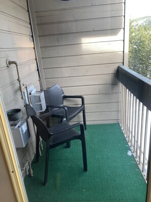 A balcony with a green mat, two black chairs, a grill, and a water heater against the wall.