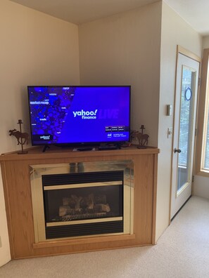 A television displaying Yahoo! Finance on a wooden entertainment unit with a fireplace below.