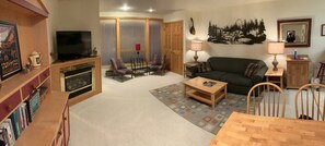A living room with a television, two armchairs, a sofa, a coffee table, and a bookshelf.