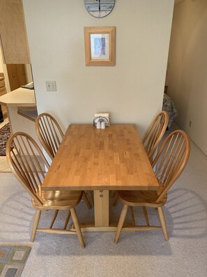 A dining area with a wooden table and four chairs, a framed picture on the wall, and a clock above the table.