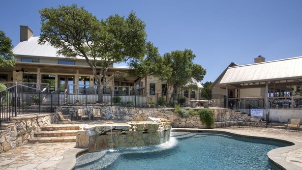 A swimming pool with a stone border, a stone waterfall feature, and a stone staircase leading to a covered area. - DREAM HOME w/ Amazing View! Movie Theater, Pool, Hot Tub, Game Room (San Marcos)