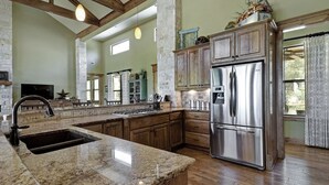 A spacious kitchen with granite countertops, wooden cabinets, and a stainless steel refrigerator. - DREAM HOME w/ Amazing View! Movie Theater, Pool, Hot Tub, Game Room (San Marcos)