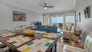 A dining area with a table set for four, a ceiling fan, and a view of the ocean through large windows.