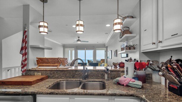 A kitchen with granite countertops, stainless steel sink, white cabinets, hanging pendant lights, and a view to the living area. - Stay & Play | 🚲 Beachfront + Bikes, Kayaks, SUP & Pool Fun on Navarre Beach 🌴 (Navarre Beach)