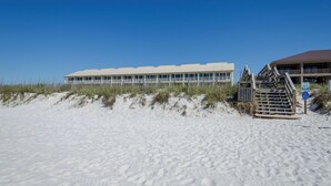 A beachfront hotel with a long building, a staircase leading to a covered area, and a sandy beach.