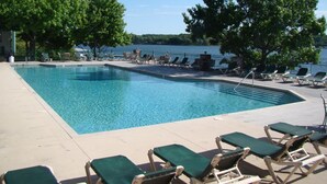 A rectangular swimming pool with a clear blue water surface, surrounded by lounge chairs and a view of a lake.
