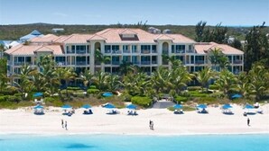 Un hôtel en bord de mer doté de nombreux balcons, d’une plage de sable et de palmiers.