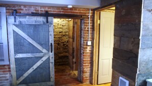 A narrow hallway with a rustic brick wall, a wooden door, and a large barn-style door.