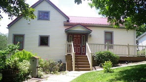 A two-story house with a red door, a front porch, and a small staircase leading to the entrance.