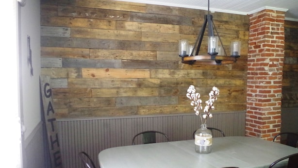 A dining area with a rustic wooden wall, a chandelier, and a table with chairs.